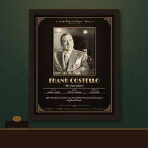 May include: A framed black and white portrait of Frank Costello in a suit, centered on a black background with gold text. The print includes the name Frank Costello, the nickname The Prime Minister, and biographical data about his life and death.