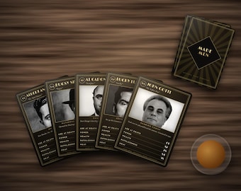 Könnte beinhalten: Ein Set Made Men Spielkarten mit schwarzen und goldenen Rändern und Porträts historischer Persönlichkeiten. Die Karten zeigen Statistiken zu Alter bei Tod, Macht, Reichtum, Rücksichtslosigkeit und Hitze. Eine kleine orangefarbene Kugel liegt daneben.