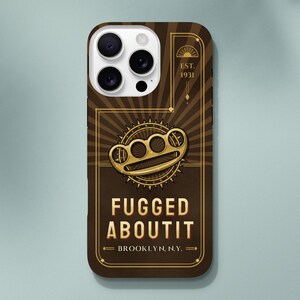 May include: A brown phone case featuring a gold-colored brass knuckle graphic centered above the text FUGGED ABOUTIT and BROOKLYN, N.Y. The design includes a sunburst pattern, a circular gear element, and the text EST. 1931 in a rectangular frame.