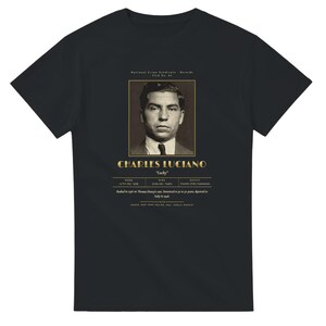 May include: A black short-sleeve t-shirt featuring a graphic print of a vintage mugshot of Charles Luciano. The design includes the text "CHARLES LUCIANO", "Lucky", and biographical details about his birth, death, and criminal history.