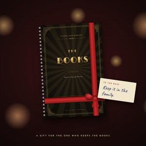May include: A black spiral-bound ledger titled THE BOOKS with gold lettering and a sunburst pattern, wrapped in a red ribbon with a gift tag that reads TO THE BOSS Keep it in the family. The bottom text reads A GIFT FOR THE ONE WHO KEEPS THE BOOKS.