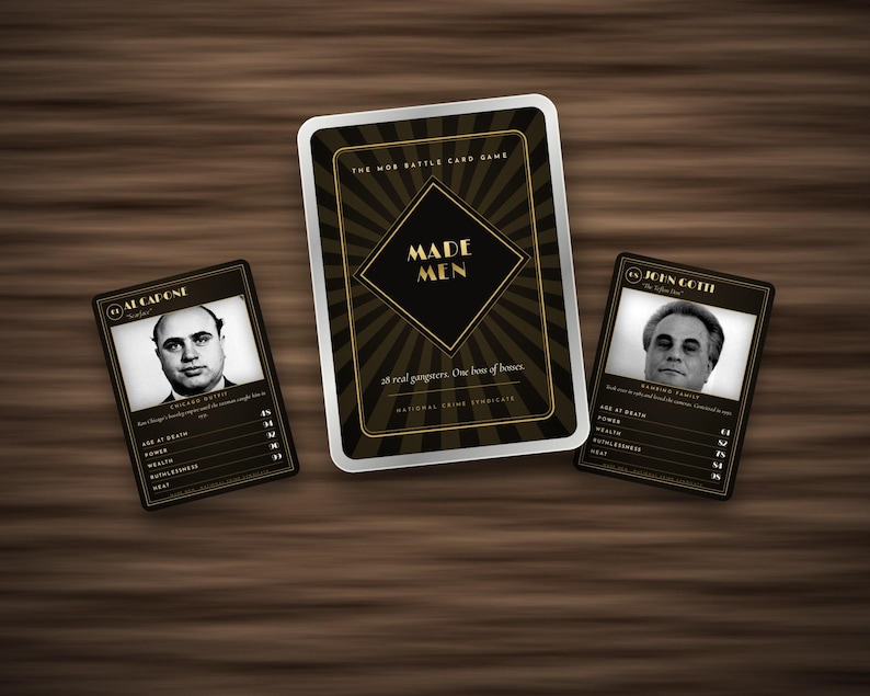 May include: A card game set titled Made Men featuring a central box with black and gold sunburst graphics, flanked by two character cards displaying black and white portraits of Al Capone and John Gotti with printed statistics and biographical text.