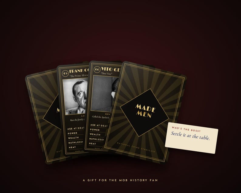 May include: A set of black and gold playing cards titled Made Men featuring historical figures like Frank Costello and Vito Genovese. The cards display statistics for age at death, power, wealth, ruthlessness, and heat. A small white card reads Who's the boss? Settle it at the table.