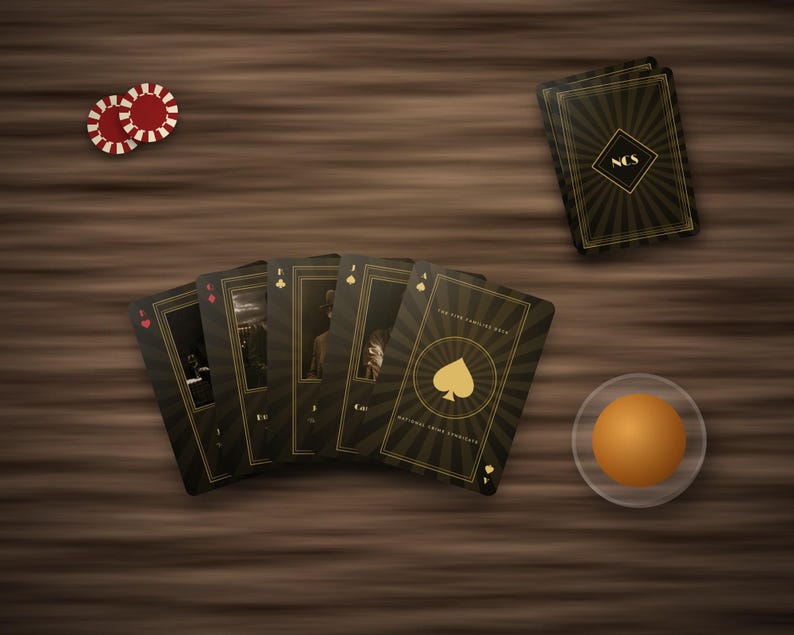 May include: A deck of black and gold playing cards with a sunburst pattern, featuring the text National Crime Syndicate. The cards are fanned out alongside two red and white poker chips and a single orange sphere on a dark wood surface.
