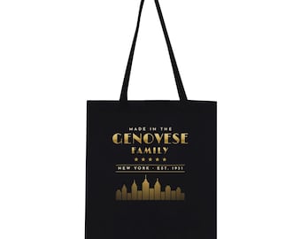 May include: A black tote bag featuring gold-colored text that reads MADE IN THE GENOVESE FAMILY, five stars, and the text NEW YORK EST. 1931 above a gold-colored graphic of a city skyline. The bag has two long black shoulder straps.