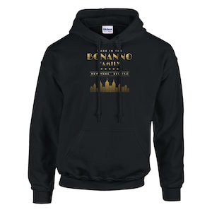 May include: A black hooded sweatshirt featuring a gold graphic print on the chest. The text reads MADE IN THE BONANNO FAMILY, NEW YORK, EST. 1931, accompanied by five stars and a gold silhouette of the New York City skyline.