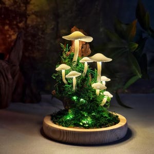 May include: A decorative mushroom lamp with glowing white mushroom caps and stems. The mushrooms are set in green moss and a wooden base. The lamp is illuminated with small green lights, creating a whimsical, fairy-tale aesthetic.