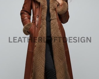 May include: A long, brown leather coat with a fur collar and trim. The coat has a button-up front and is worn over a black top and pants. The text "LEATHERUFTDESIGN" is visible on the coat. The model is wearing brown boots.