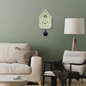 Peut inclure: Une horloge à coucou vert clair avec un pendule et un poids noirs. L'horloge a la forme d'une maison avec une petite ouverture en haut. L'horloge est fixée sur un mur vert. Ses dimensions sont d'environ 25 cm de hauteur.