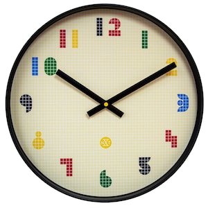 Op de afbeelding: Een ronde wandklok met een zwart frame en een crèmekleurige wijzerplaat. De wijzerplaat heeft een rasterpatroon en kleurrijke, gepixelde cijfers. De wijzers zijn zwart en de klok heeft een klein logo in het midden.