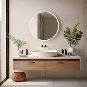A modern bathroom vanity features a round white mirror and a light wood floating cabinet with two drawers. A white oval sink sits atop the cabinet.