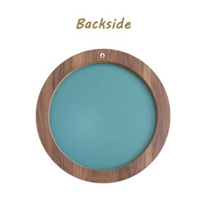 backside of the mirror. Round wooden frame with a teal center. The frame has a natural wood grain finish and a small hole at the top for hanging. The word "Backside" is printed in a brown script font above the frame.
