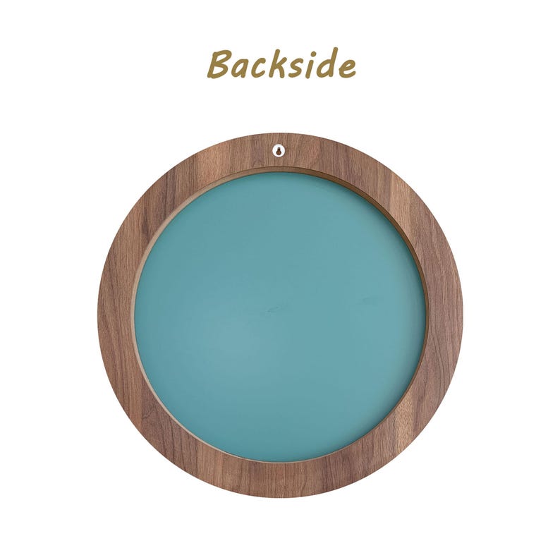 backside of the mirror. Round wooden frame with a teal center. The frame has a natural wood grain finish and a small hole at the top for hanging. The word "Backside" is printed in a brown script font above the frame.
