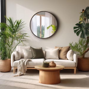 A living room scene featuring a light-colored sofa with several pillows in neutral tones. A large round mirror hangs above the sofa.