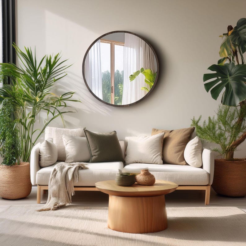 A living room scene featuring a light-colored sofa with several pillows in neutral tones. A large round mirror hangs above the sofa.