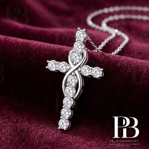 May include: A silver-toned cross pendant necklace featuring a vertical row of round, clear, faceted stones intersected by a polished metal infinity-style loop. The cross is adorned with additional round stones along the horizontal arms.