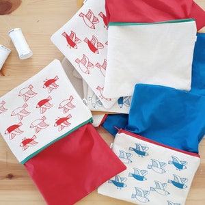 May include: Five zippered pouches with a red, white, and blue color scheme. Each pouch features a repeating pattern of stylized birds. The pouches are made of a soft, fabric material.