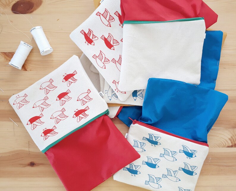 May include: Five zippered pouches with a red, white, and blue color scheme. Each pouch features a repeating pattern of stylized birds. The pouches are made of a soft, fabric material.