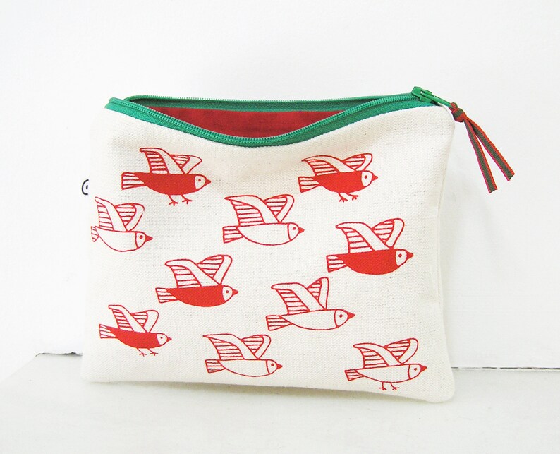 May include: A white canvas zippered pouch with a red and green zipper and a red and white bird print. The birds are stylized and have a simple design.