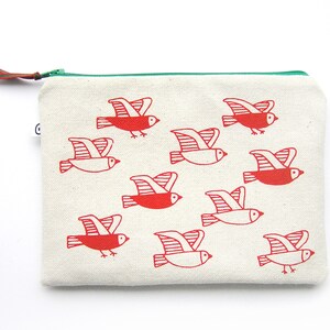 May include: A white canvas zippered pouch with a green zipper pull. The pouch is decorated with a repeating pattern of red stylized birds in flight.
