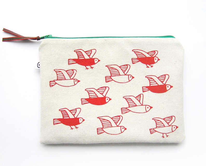 May include: A white canvas zippered pouch with a green zipper pull. The pouch is decorated with a repeating pattern of red stylized birds in flight.