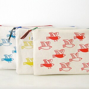 May include: Four zippered pouches with different colored bird designs. The pouches are made of white canvas and have a zipper closure. The birds are printed in blue, yellow, and red.