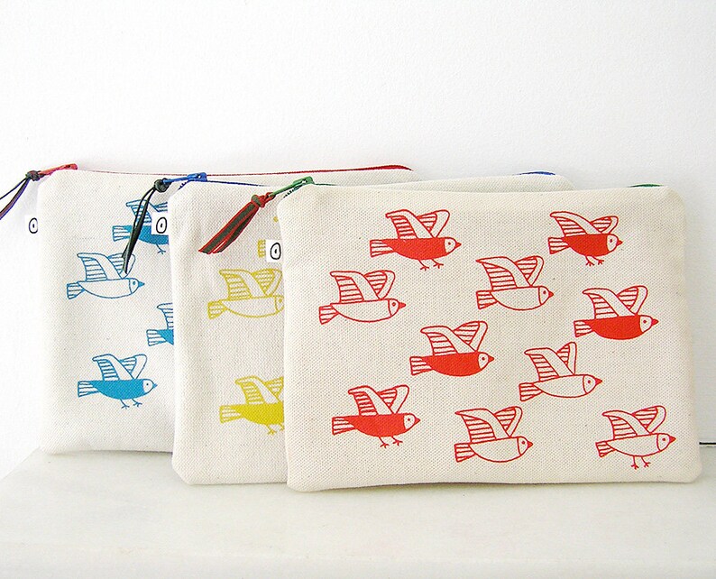 May include: Four zippered pouches with different colored bird designs. The pouches are made of white canvas and have a zipper closure. The birds are printed in blue, yellow, and red.