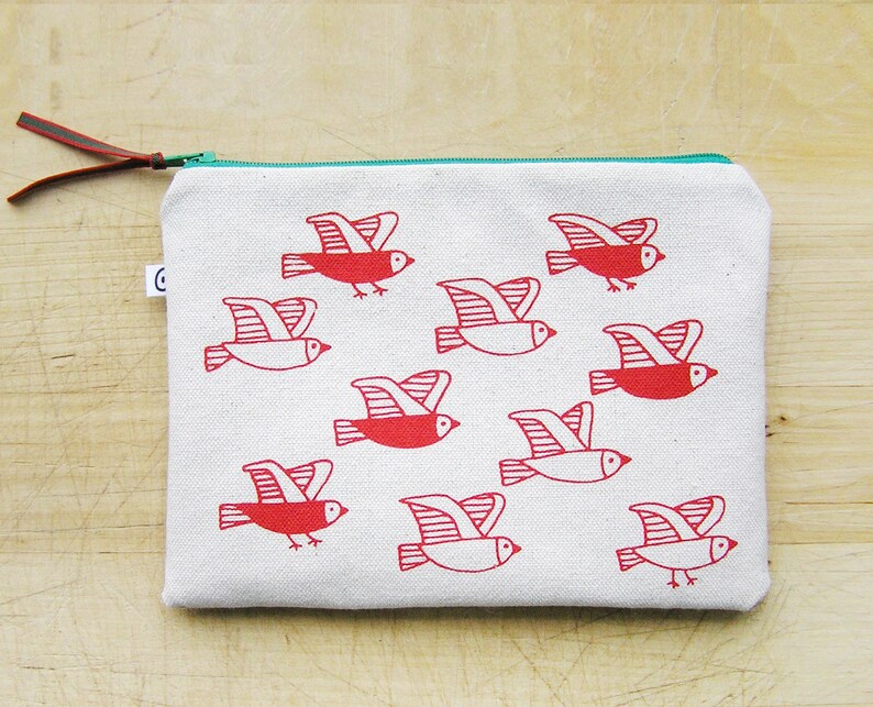 May include: A white canvas zippered pouch with a red and white bird design. The birds are flying in different directions. The zipper is teal.