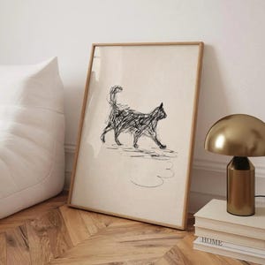 Könnte beinhalten: Ein gerahmter Kunstdruck mit einer schwarzen Strichzeichnung einer Katze. Das Kunstwerk ist vor einem cremefarbenen Hintergrund platziert und in einem hellbraunen Holzrahmen gerahmt. Der Druck wird auf einem Holzboden präsentiert.