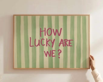 May include: A framed art print with a light green and cream striped background. The text "HOW LUCKY ARE WE?" is written in pink. The frame is a light brown color.