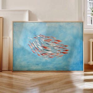 Puede incluir: Una obra de arte enmarcada que representa un banco de peces nadando en un patrón circular. Los peces son una mezcla de blanco y naranja sobre un fondo azul claro, creando una sensación de movimiento y profundidad. La obra se exhibe en una habitación con suelo de parquet.