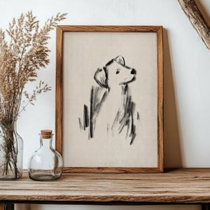Puede incluir: Un boceto a carboncillo enmarcado de un perro, en blanco y negro. La obra de arte presenta un estilo minimalista, con el perfil del perro mirando hacia arriba. El marco es de madera. La obra se exhibe sobre una superficie de madera.