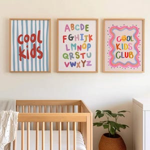 May include: Three framed art prints with a children's theme. One print has blue and white vertical stripes with the words "cool kids" in red. Another features the alphabet in colorful letters. The third print says "cool kids club" with a smiley face.