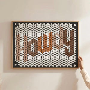 May include: Framed wall art with the word "SUN" in a mosaic design. The artwork uses a honeycomb pattern with shades of brown, white, and orange. It is set against a black border and a natural wood frame.
