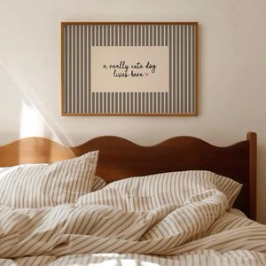以下が含まれることがあります： 「a really cute dog lives here」のテキストが入った額入りのプリントが寝室に飾られています。プリントは茶色のフレームとストライプの背景です。ベッドにはストライプの寝具と木製のヘッドボードがあります。