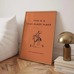 May include: Framed art print with an orange background and a cowboy illustration. The text reads "THIS IS A HIGH CLASS PLACE" and "ACT RESPECTABLE". The artwork is in a wooden frame.