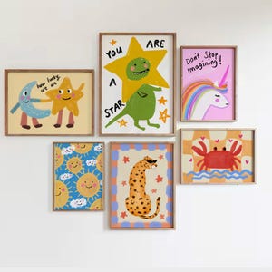 May include: A collection of framed art prints featuring whimsical illustrations. The artwork includes a yellow star with a green creature, a unicorn, a crab, a cheetah, smiling suns, and a moon and star. Text includes "You are a star" and "Don't Stop Imagining!"