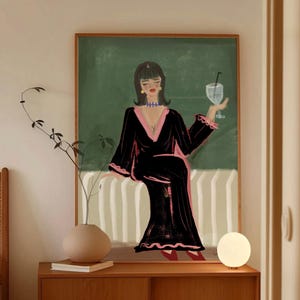 Pode incluir: Uma impressão artística com uma mulher em um vestido preto com acabamento rosa, segurando um coquetel. A obra de arte é definida em um fundo verde com um padrão de listras brancas e verdes. A impressão é emoldurada em uma moldura de madeira.