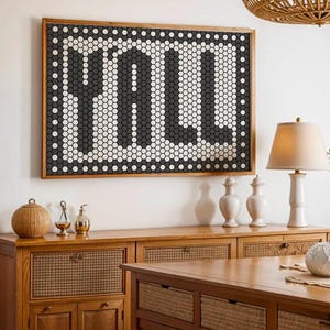 May include: A framed artwork spelling "FULL" in a mosaic of black, white, and grey hexagonal tiles. The wooden framed art hangs above a wooden cabinet. The room is decorated with a lamp, vases, and decorative objects, creating a stylish interior design.