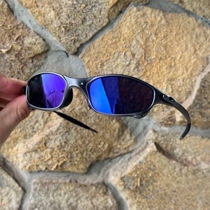 May include: A pair of sunglasses with a dark gray frame and blue mirrored lenses. The sunglasses have a sleek, modern design with curved temples and a minimalist aesthetic. The lenses reflect a vibrant blue hue.