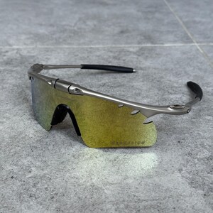 May include: Silver-framed sunglasses with a yellow-green gradient lens. The sunglasses have a sleek, modern design with black ear pieces. The lenses are a vibrant yellow-green color, and the frame is a metallic silver.