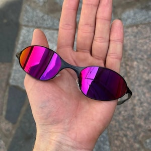May include: Oval-shaped sunglasses with black frames and pink and purple mirrored lenses. The lenses reflect a range of colours. A contemporary eyewear accessory.