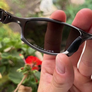 May include: Close-up of a pair of gray sunglasses with dark lenses. The sunglasses have a sleek, modern design with a metal frame and black nose pads. The word "POLARIZED" is printed on the lens.
