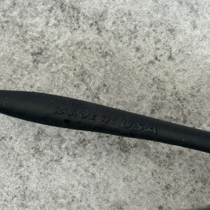 May include: Close-up of a black object with the embossed text "MADE IN USA". The object appears to be a part of a larger item, possibly eyewear or a similar product. The background is a textured gray surface.