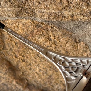 May include: Close-up of silver-toned sunglasses with the text "Polarized 004008DART 133 130" printed on the arm. The sunglasses feature a decorative design on the frame and a black arm tip.
