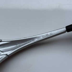 May include: A silver-colored tool with the text "MADE IN U.S.A." printed on the surface. The tool has a black rubber grip on one end.
