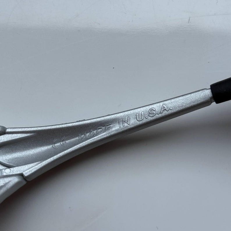 May include: A silver-colored tool with the text "MADE IN U.S.A." printed on the surface. The tool has a black rubber grip on one end.