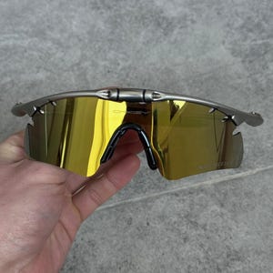 May include: Silver-framed sunglasses with gold-tinted lenses. The sunglasses have a black nose bridge and ear pieces. The lenses are a bright gold color, and the frame is a metallic silver.