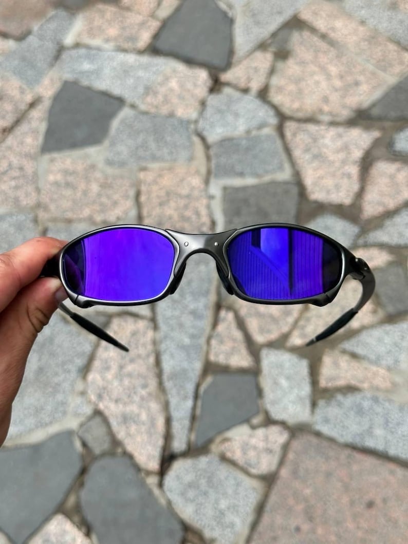 May include: Black sunglasses with purple mirrored lenses. The sunglasses have a sleek, modern design with a dark frame and curved temples. The lenses reflect a vibrant purple hue, offering a stylish and functional accessory.