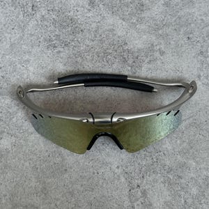 May include: Silver-framed sunglasses with iridescent lenses. The sunglasses have a black nose bridge and ear pieces. The lenses have a gradient of colors, and the frame is a metallic silver color. The sunglasses are designed for sports and outdoor activities.